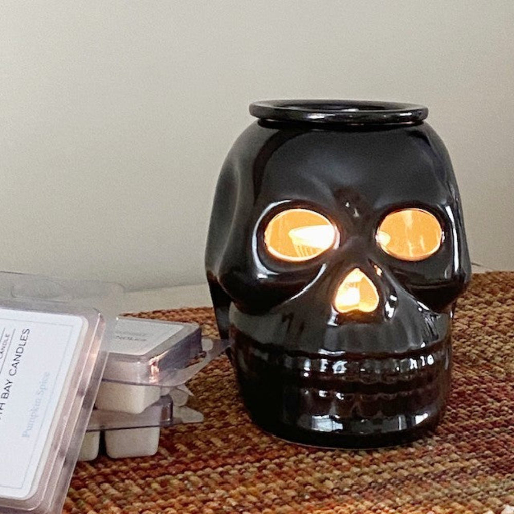 Black skull shaped candle warmer with on a textured fall surface.