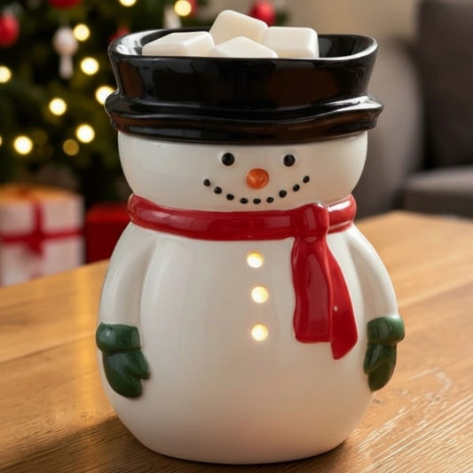 Snowman wax fragrance warmer on a table with a Christmas tree in the background.