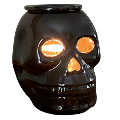 Black skull Halloween candle warmer with glowing eyes white background.