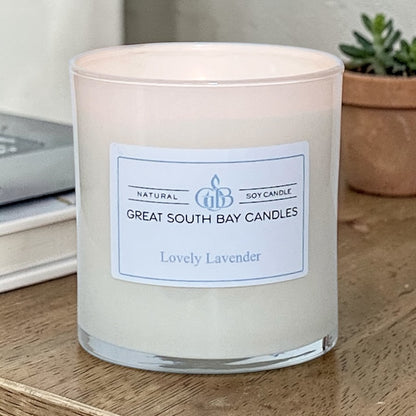 Great South Bay Candles Lovely Lavender candle on a wooden surface with a plant in the background