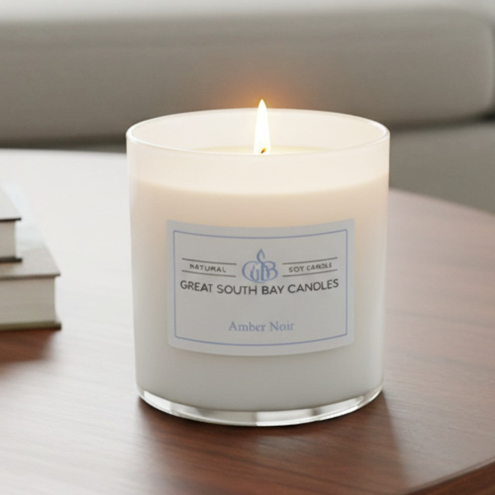 Warm glow of a lit of a 8oz Amber Noir candle on a wooden living room. table.