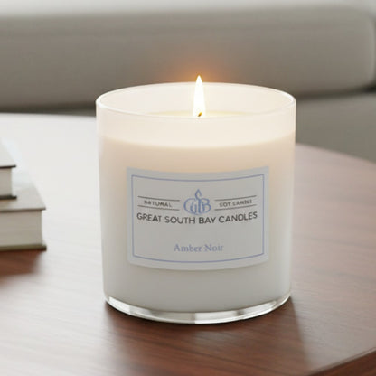 Warm glow of a lit of a 8oz Amber Noir candle on a wooden living room. table.