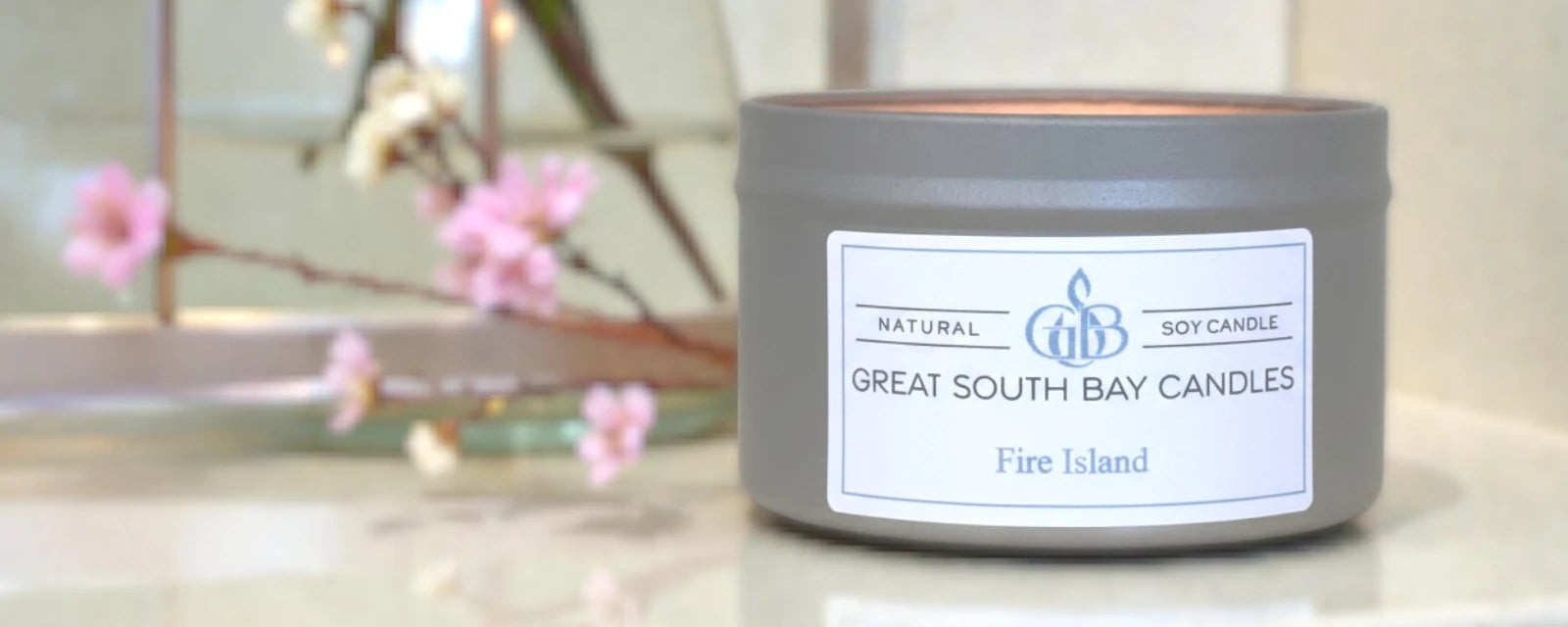 Fire Island beach scented candle on a grey surface with florals in background.