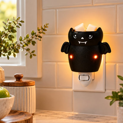 A black bat candle wax melt warmer. Shown lit in a kitchen setting with tiled walls and plants.