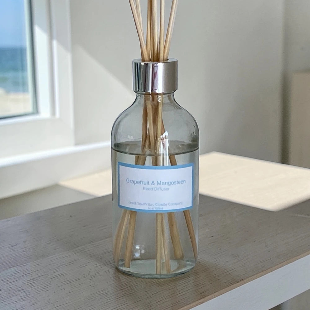 Glass diffuser bottle with rattan reeds on a wooden surface near a window.